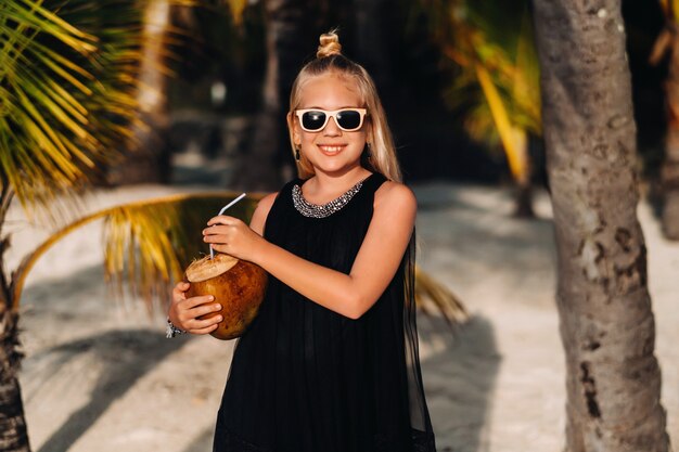 Retrato de uma menina alegre de 9 anos com um coquetel de coco no fundo de palmeiras em uma praia exótica. menina com um coco na praia da ilha de maurício