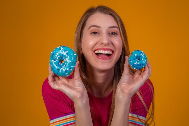 Retrato de uma menina alegre e bonita segurando rosquinhas azuis na frente do rosto