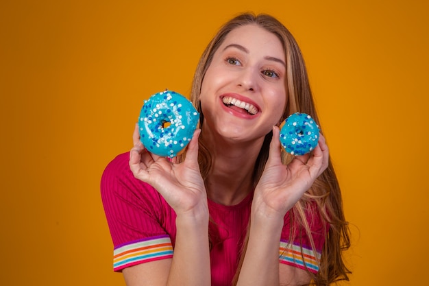 Retrato de uma menina alegre e bonita segurando rosquinhas azuis na frente do rosto