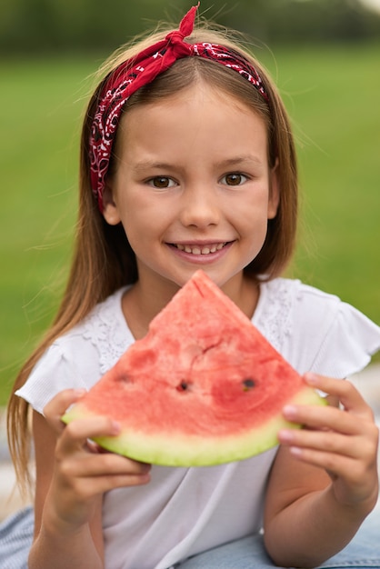 Retrato de uma menina alegre olhando para a câmera enquanto segura uma família de fatias de melancia, tendo um