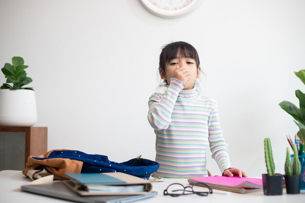 Retrato de uma menina asiática doente e insalubre com sintomas de gripe tossindo mantendo a mão perto da boca