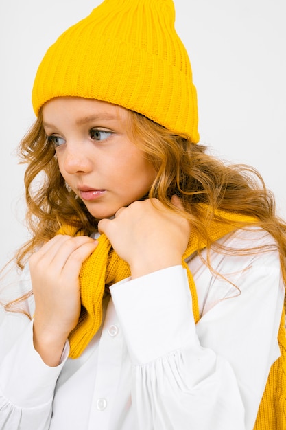 Retrato de uma menina atraente em um chapéu amarelo e uma camisa branca com uma camisola de malha nos ombros