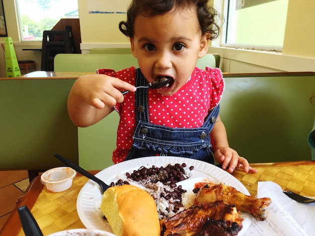 Foto retrato de uma menina bebê comendo com colher em casa