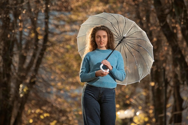 Retrato de uma menina bonita com cabelo comprido no parque outono Jovem mulher de suéter com guarda-chuva transparente no parque outono