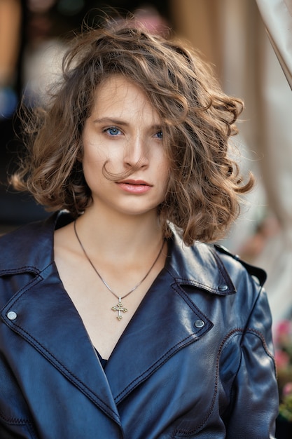 Retrato de uma menina bonita com cabelo encaracolado selvagem em pé perto de terraço em casaco longo