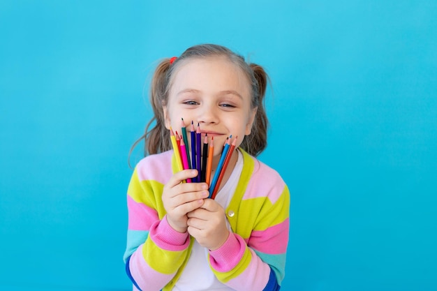 retrato de uma menina bonita com lápis coloridos em uma jaqueta listrada o conceito de educação e desenho estúdio de fotos fundo azul lugar para texto