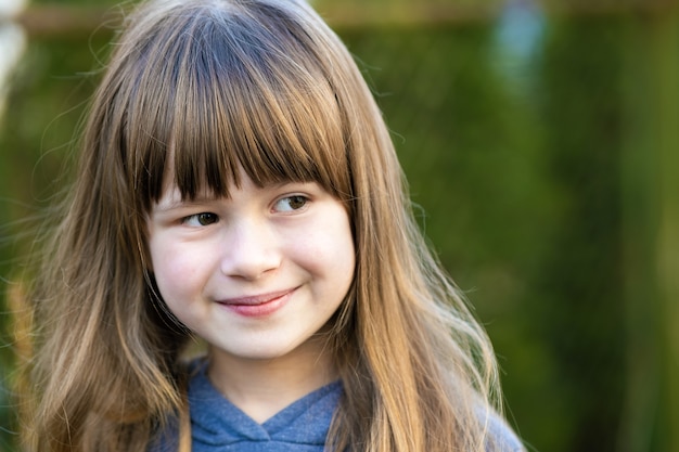 Retrato de uma menina bonita com olhos cinzentos e cabelo longo loiro sorrindo ao ar livre