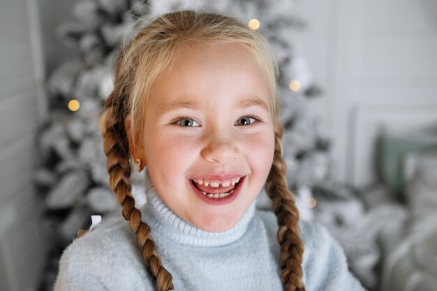 Retrato de uma menina bonita com rabo de cavalo no contexto de uma árvore de Natal com luzes de guirlanda. Foco seletivo, fundo desfocado.