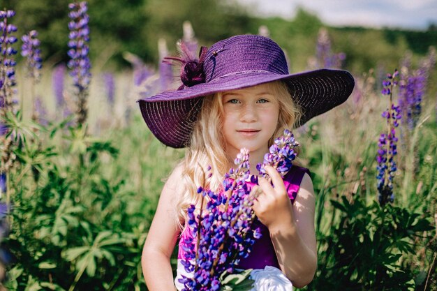 Retrato de uma menina bonita com um chapéu violeta com buquês de tremoços no rosto