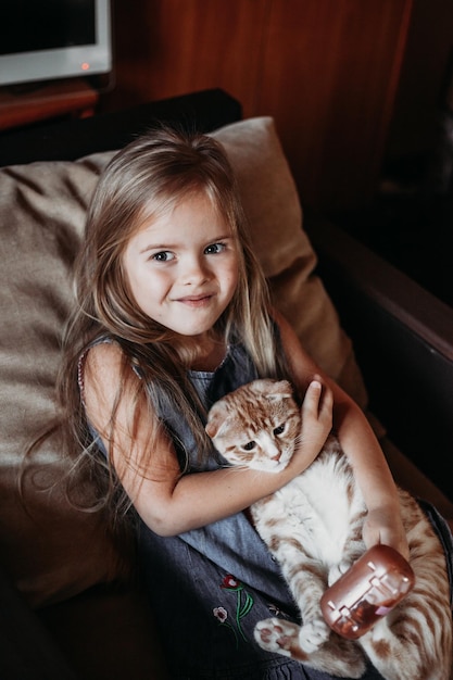 Retrato de uma menina bonita com um gato sentado em uma cadeira em casa