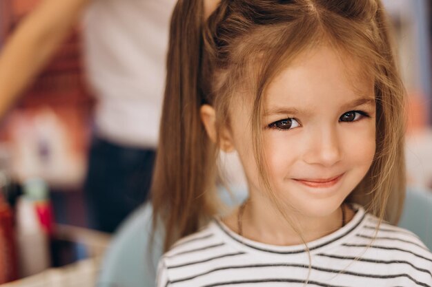 Retrato de uma menina bonita com um penteado elegante em um salão de beleza expressando felicidade da criança bonita