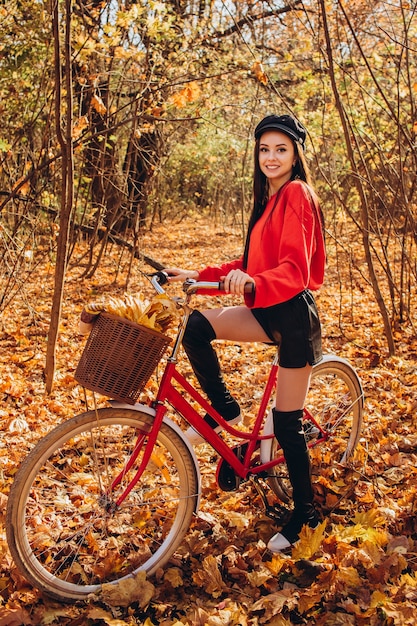 Retrato de uma menina bonita com uma bicicleta vermelha na floresta de outono