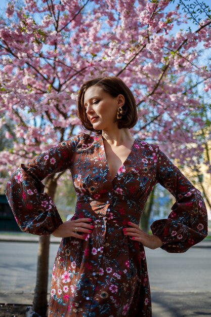 Foto retrato de uma menina bonita e bonita em um vestido no jardim, no meio de uma floração de sakura. primavera e sol. fundo desfocado e foco selecionado.