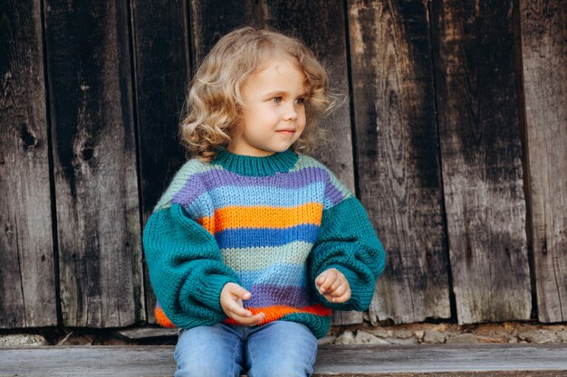 Retrato de uma menina bonita e feliz encaracolada com uma camisola de malha perto de uma parede de madeira