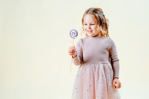 Retrato de uma menina bonita em um fundo claro com um pirulito na mão. Conceito de comida