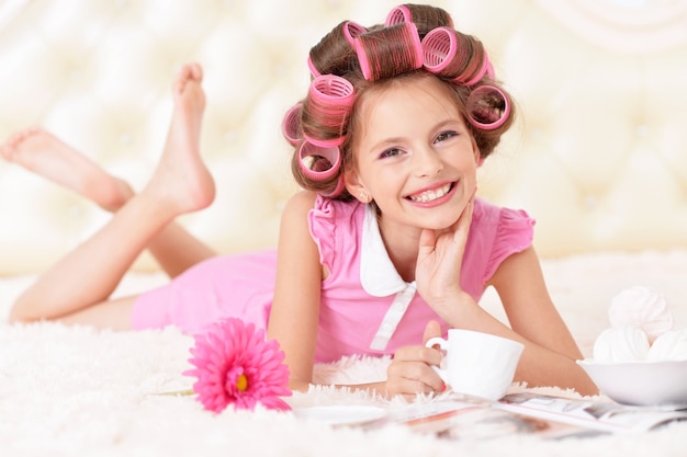 Retrato de uma menina bonita feliz com rolos de cabelo com chá