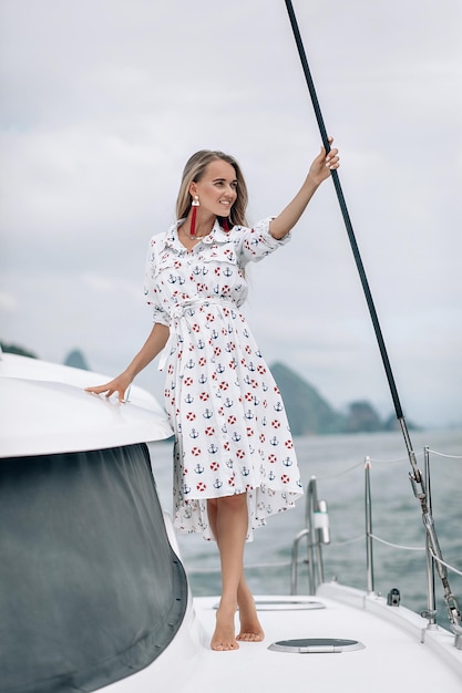 Retrato de uma menina bonita feliz com vestido branco e cabelo loiro longo encaracolado em pé no iate no verão. olhando para a câmera com um sorriso dentuço.