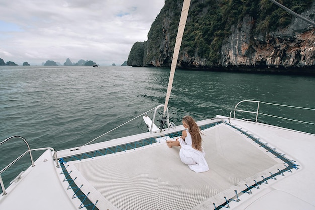 Retrato de uma menina bonita feliz com vestido branco e cabelo loiro longo encaracolado, sentado no iate no verão. olhando para o mar. Phuket. Tailândia