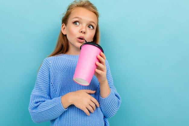 Retrato de uma menina bonita pensativa com um copo de café sobre um fundo azul