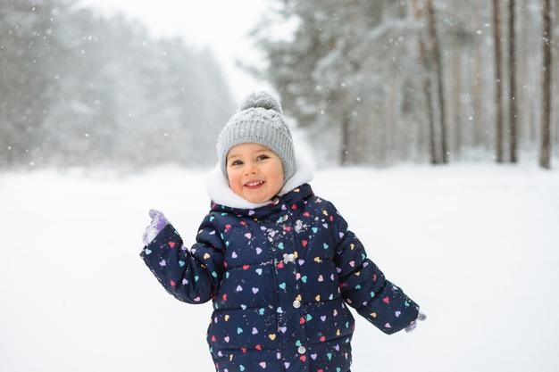 Retrato de uma menina bonita se divertindo brincando ao ar livre durante a queda de neve