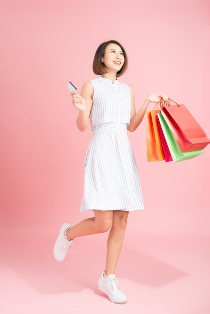 Retrato de uma menina bonita sorridente em um vestido com sacolas de compras, segurando um cartão de crédito isolado sobre um fundo rosa