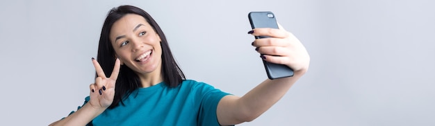 Retrato de uma menina bonita tirando uma selfie isolada sobre fundo cinza