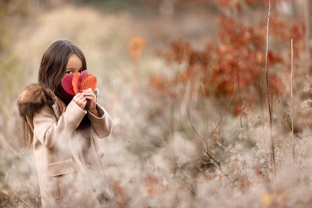 Retrato de uma menina bonitinha brincando com folhas caídas de outono