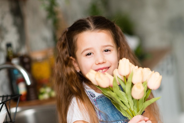 Retrato de uma menina bonitinha com flores em um vestido azul jeans. Retrato de primavera. Dia das Mães.