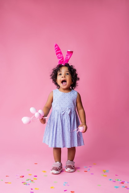 retrato de uma menina bonitinha com orelhas de coelhinho da Páscoa na cabeça segurando ovos de Páscoa. estúdio, fundo rosa