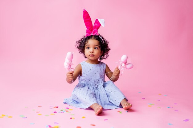 retrato de uma menina bonitinha com orelhas de coelhinho da Páscoa na cabeça segurando ovos de Páscoa. estúdio, fundo rosa