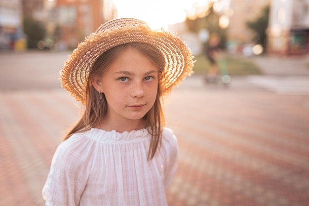 Retrato de uma menina bonitinha com sardas em um chapéu de palha ao pôr do sol
