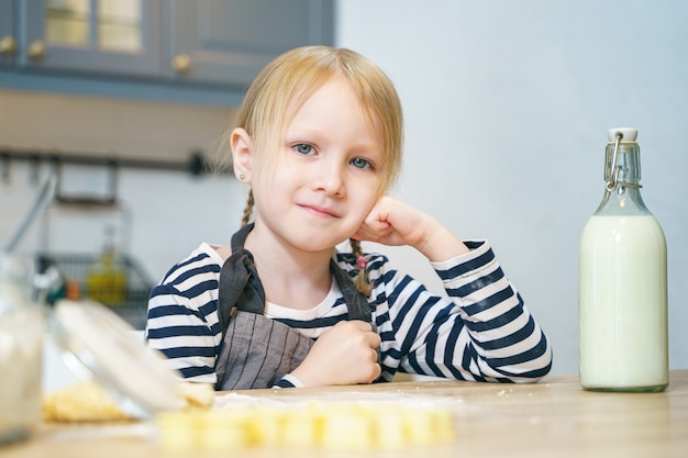Retrato de uma menina bonitinha com um avental, preparando a massa para biscoitos na cozinha.