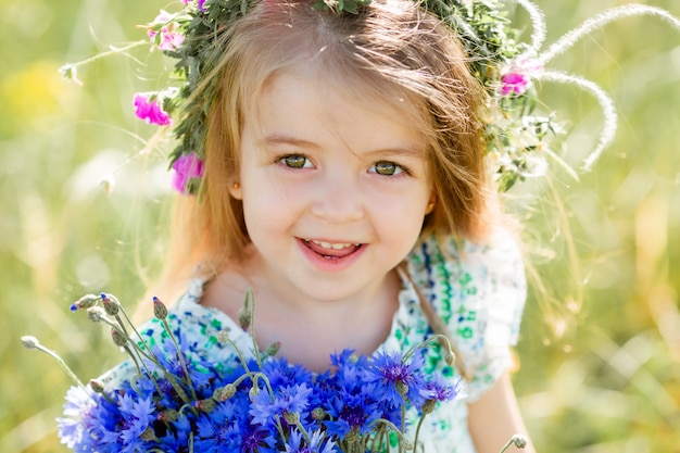 Retrato de uma menina bonitinha com uma coroa na cabeça sorrindo segurando flores silvestres de centáurea