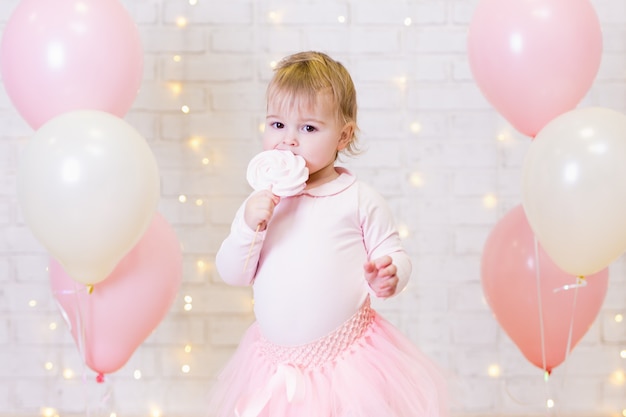 Retrato de uma menina bonitinha comendo doces sobre um fundo de parede de tijolos com luzes e balões