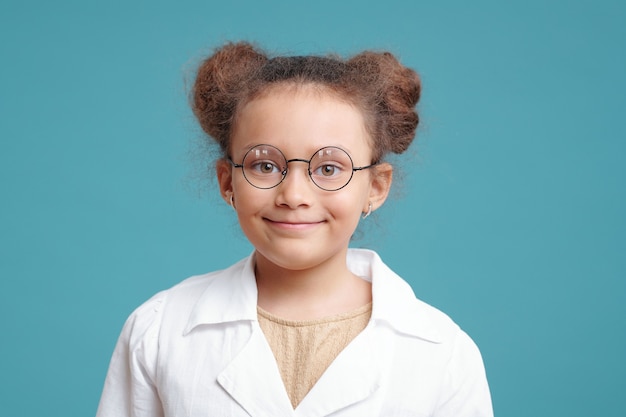 Retrato de uma menina bonitinha em óculos, sorrindo para a câmera contra o fundo azul