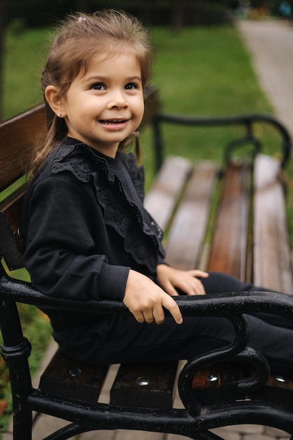 Retrato de uma menina bonitinha em um lindo terno preto sentado no banco, clima de outono