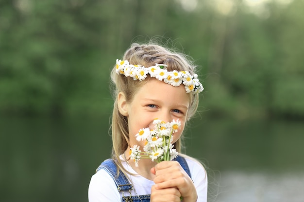 Retrato de uma menina bonitinha em uma coroa de flores e um buquê de f selvagem