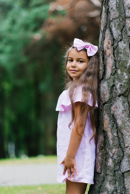 Retrato de uma menina bonitinha encostada em uma grande árvore com as costas na floresta no verão