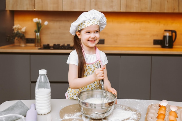 Retrato de uma menina bonitinha parada em uma cozinha moderna e preparando massa