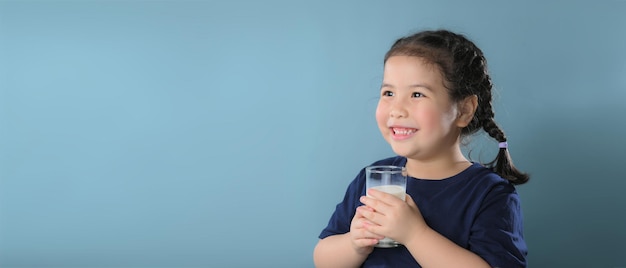 Retrato de uma menina bonitinha satisfeita com copo de leite isolado sobre fundo azul.