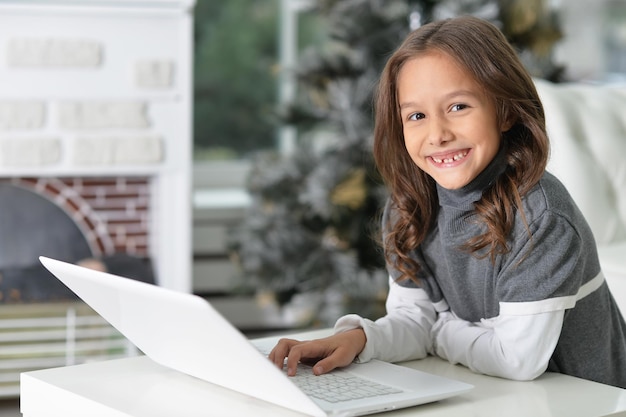 Retrato de uma menina bonitinha sentada à mesa com o laptop