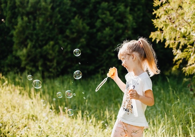 Retrato de uma menina bonitinha soprando bolhas de sabão no parque no verão