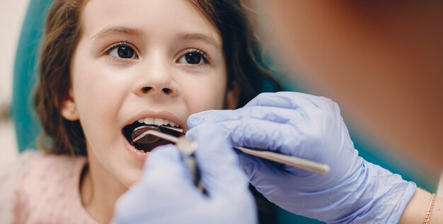 Retrato de uma menina bonitinha, tendo um exame de dentes em estomatologia pediátrica, enquanto olha para o médico.