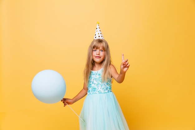 Retrato de uma menina bonito em um chapéu festivo e com balões em um fundo amarelo.