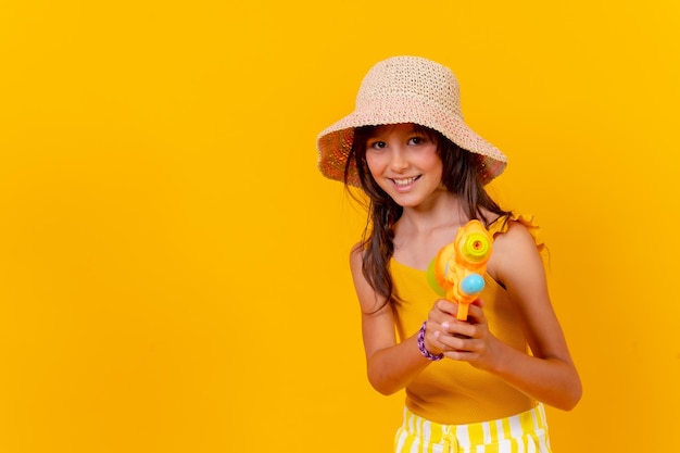 Retrato de uma menina brincando com uma pistola de água no fundo amarelo de férias de verão