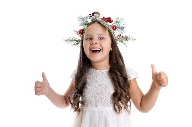 Retrato de uma menina caucasiana alegre e satisfeita com vestido branco de guirlanda de Natal e dando polegares para cima iso ...