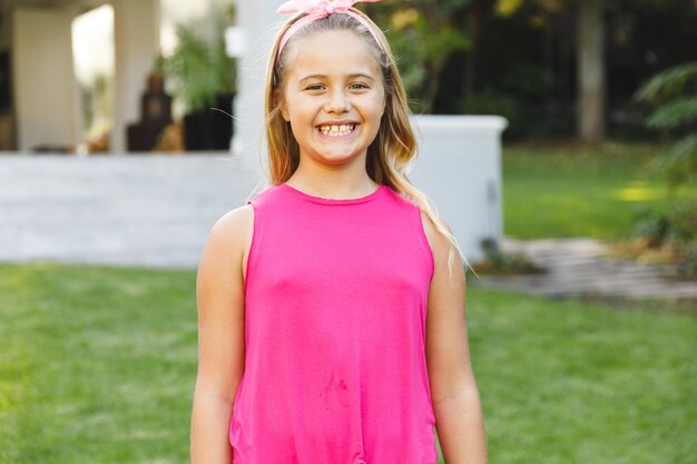 Foto retrato de uma menina caucasiana sorridente do lado de fora de casa, olhando para a câmera no jardim