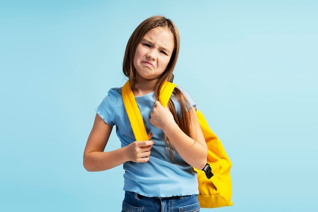 Retrato de uma menina chorando, vestindo roupas casuais, uma mochila e olhando para a câmera.