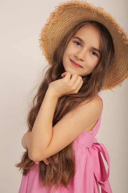 retrato de uma menina com cabelo comprido em um vestido de linho rosa e um chapéu de palha