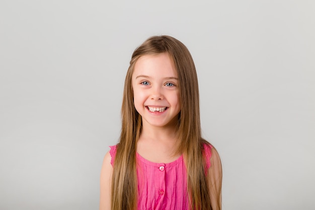 Retrato de uma menina com cabelos compridos em roupas cor de rosa. menina feliz sorrindo no espaço em branco isolado